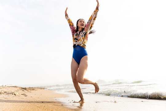 Happy woman raising arms while enjoying beach at sunrise - Powered by Adobe
