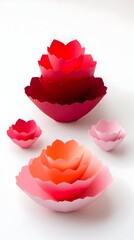 Two sets of nested, petal-shaped bowls in varying shades of pink and red, crafted from a paper-like material, are displayed against a bright white backdrop.  The bowls are arranged in a visually