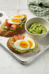 Smoked Salmon toast with Avocado and lime cream. Sesame seeds bread, boiled egg. Close up of homemade sandwich. Vertical image, copy space.