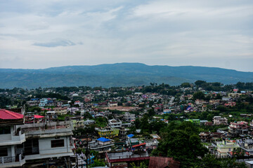 Fototapeta premium Panoramic view of a bustling hillside town near Shillong with diverse architecture under a cloudy sky.