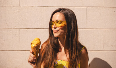 Attractive long brunette hair woman hold ice cream and look on it with desire, wear yellow...