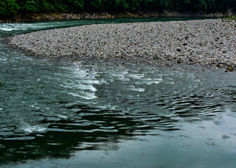 Rocky riverbank next to flowing water, with reflections on the surface in Meghalaya. 