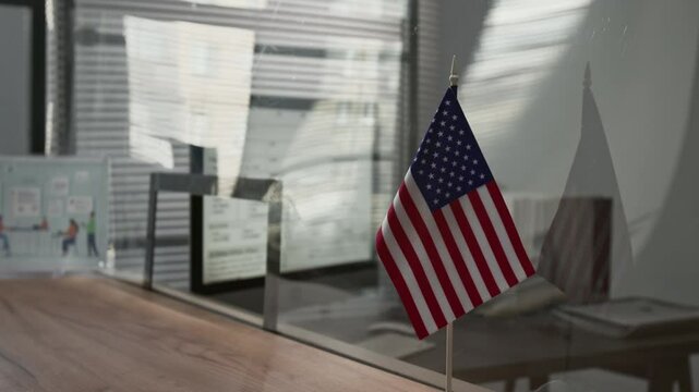 Close-up selective focus shot of small American flag on wooden top of service desk with glass partition in visa center
