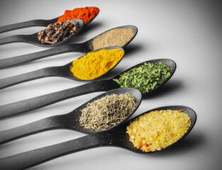 Assorted colorful spices on black spoons close-up