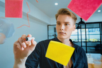 Professional caucasian businessman writing marketing idea by using mind map and sticky notes on glass board at modern meeting room. Creative business and planing concept. Closeup. Immaculate.