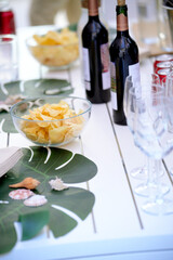 Potato chips, wine bottles, and seashells decorating a white table for a summer party