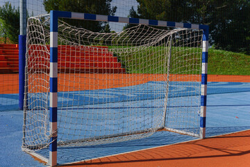 blue and white striped handball goal on outdoor court, diverse colored flooring, concept of sports...