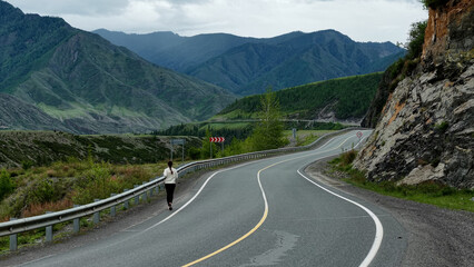 Runner in the mountains. A woman runs along a mountain road, high mountains in the background. Tourism in the Altai Mountains. Fitness while traveling.
