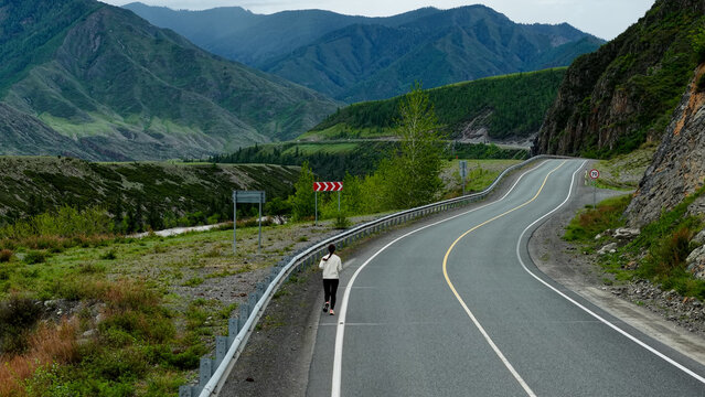 Runner in the mountains. A woman runs along a mountain road, high mountains in the background. Tourism in the Altai Mountains. Fitness while traveling. - Powered by Adobe