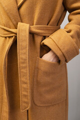Close-up of a person inserting a hand into the pocket of a cozy brown wool coat. The texture...