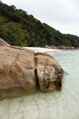 Coastal scene featuring large rocks leading into clear water, adjacent to a pristine sandy beach...