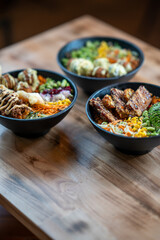 Three poke bowls with assorted ingredients, front view, isolated on wooden table background.