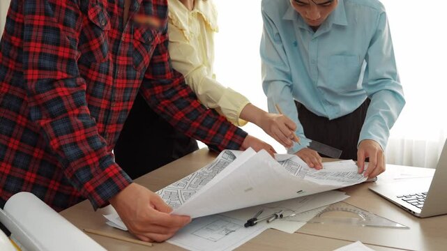 Professional engineer team discussion about house design on meeting table with architectural equipment and building blueprint scatter around at modern office. Focus on hand. Closeup. Delineation.