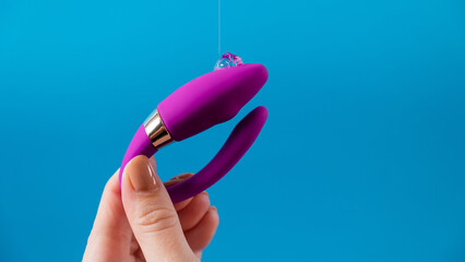 A woman holds a curved sex toy in lubrication on a blue background. Vaginally clitoral vibrator. 