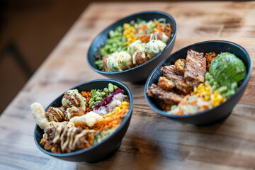 Three poke bowls with grilled meat and vegetables, front view, isolated on wooden background.