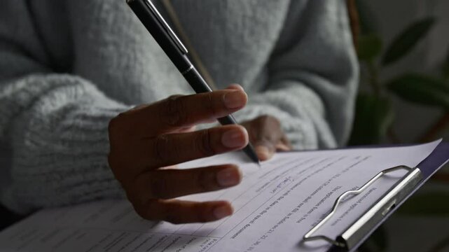 Close-up view of hand of unrecognisable Black young woman filling in visa application form holding clipboard and pen