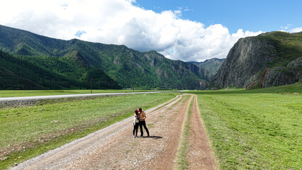 Fototapeta premium A couple travels through the Altai Republic. A couple kisses while walking along the road against the backdrop of mountains. Mountain trips for two. Traveling around Russia.