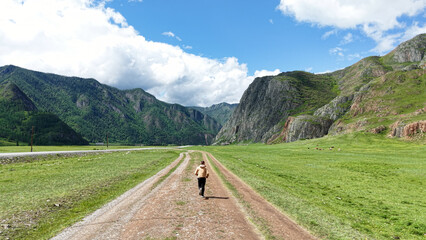 Fototapeta premium A man takes a selfie with a drone while traveling in the mountains. A man walks along a road in the mountains, filming himself with a drone. Traveling in Altai. Traveling in Russia.