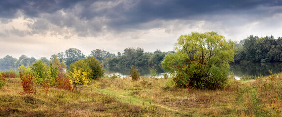 Autumn river landscape with colorful trees and bushes under a cloudy sky