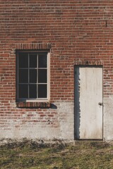 In a picturesque rural setting, a weathered brick wall features a charming window and an antique white door, all illuminated by daylight, highlighting the beauty of vintage architecture