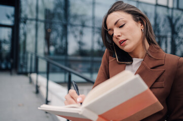 Businesswoman writing notes while talking on phone outside office