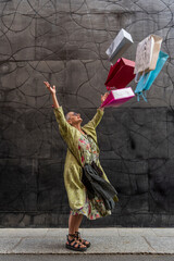 elegant mature woman having fun throwing colorful shopping bags up in front of a black wall