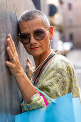 portrait of beautiful mature woman with colorful shopping bags leaning against black wall in street