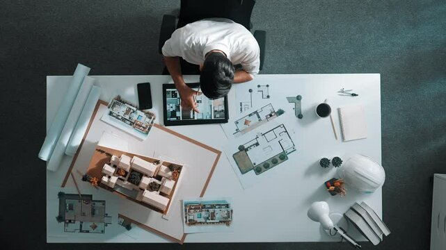 Top view of business man using tablet plan house design while sitting at meeting table with blueprint and equipment scatter around. Aerial view of civil engineer working at blueprint. Alimentation.