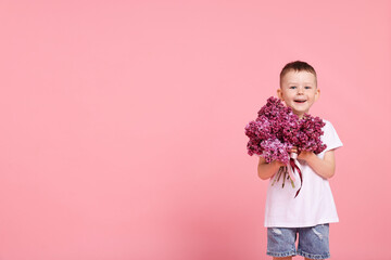 Little boy with bouquet of lilac flowers on pink background, space for text