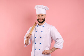 Happy confectioner in uniform holding rolling pin on pink background