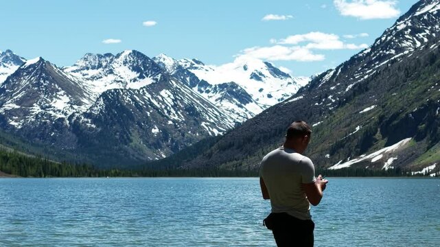 Cinematic views of a mountain lake with high mountains. Multinsky lakes are high-mountain lakes in the Altai Mountains. A man takes a selfie during a trip to the Altai Mountains.