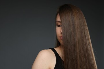 Naklejka premium Teenage girl with healthy long hair on dark grey background. Space for text