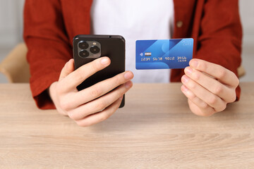 Woman with credit card and smartphone paying online at wooden table, closeup