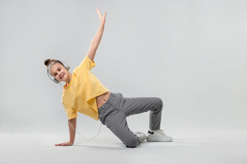 Girl with headphones in stylish clothes dancing on light grey background
