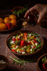 Chef pouring balsamic vinegar onto fresh summer salad with strawberries and cheese
