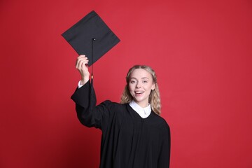 Happy student with mortarboard after graduation on red background
