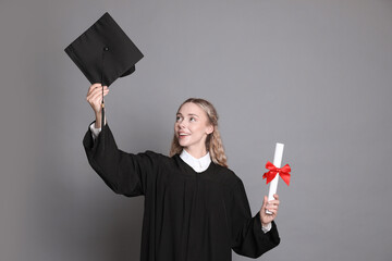 Happy student with diploma and mortarboard after graduation on grey background