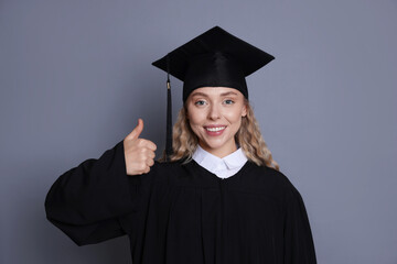 Happy student after graduation showing thumbs up on grey background