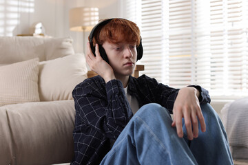 Obraz premium Teen problems. Depressed teenage boy listening to music on floor at home