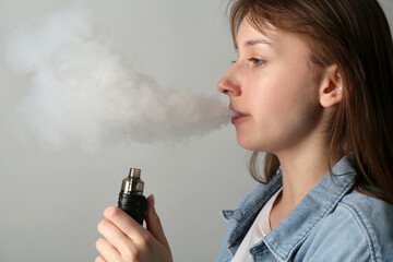 Woman using electronic smoking device on light grey background