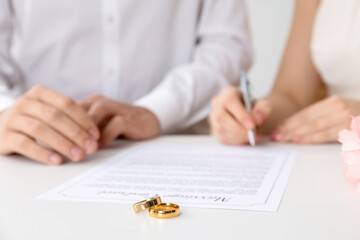 Newlyweds signing marriage contract and wedding rings on desk, selective focus