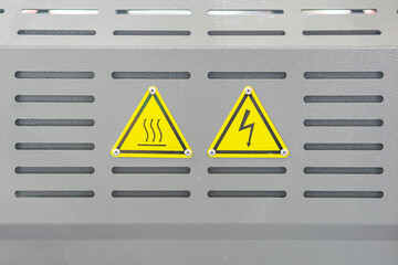 Close-up of two warning signs on an appliance or electronic device, depicting hot surface and...