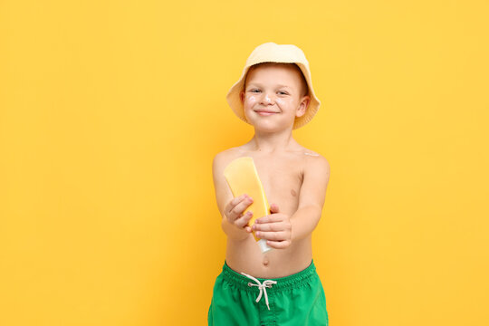 Little boy with tube of sun protection cream on yellow background