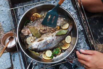 Person grilling vegetables, sausages, chicken, trout over charcoal in a backyard during summer. Outdoor cooking with real flames and smoke in a cozy home setting