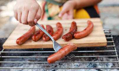 Person grilling vegetables, sausages, chicken, trout over charcoal in a backyard during summer. Outdoor cooking with real flames and smoke in a cozy home setting