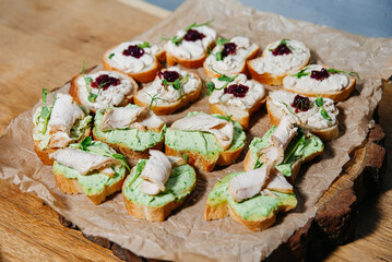 Chicken Crostini with Cream Spread and Garnish. Assorted crostini topped with sliced chicken breast, creamy herb spread, and cranberry sauce, served on rustic parchment paper.