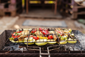 Person grilling vegetables, sausages, chicken, trout over charcoal in a backyard during summer. Outdoor cooking with real flames and smoke in a cozy home setting