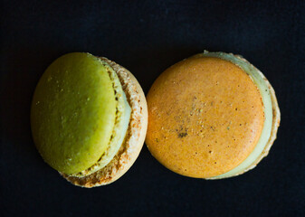 Closeup photography of two macarons on a dark background: one green and one orange. Still nature in the kitchen.