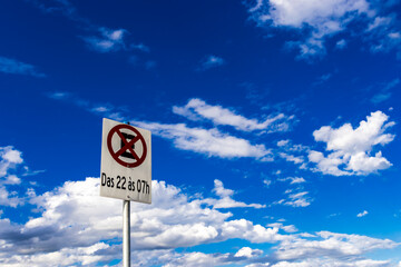 No parking sign between 10pm and 7am with a blue sky with clouds in the background, in Brazil