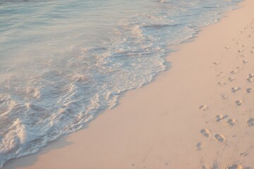 Golden hour at the beach with gentle waves washing over soft sand and footprints leading towards the tranquil water